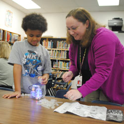 Teacher's aide stands next to a student as they do an activity