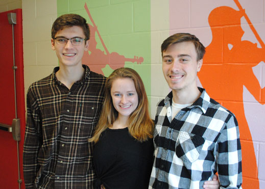 Three students pose against a mural