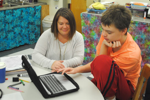 Teacher aide looks on as student uses laptop computer