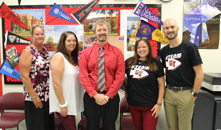 five school cpunseling staff members in a line smiling in front of bulletin board with college pennants