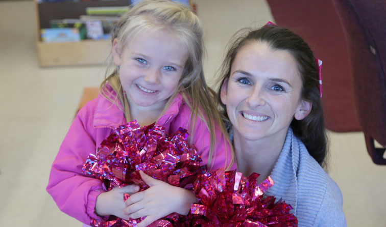 elementary student and teacher holding pink sparkle pom-poms smiling