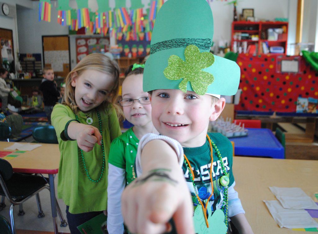 three pre-K students dressed in St. Patricks day green smile and point at the viewer