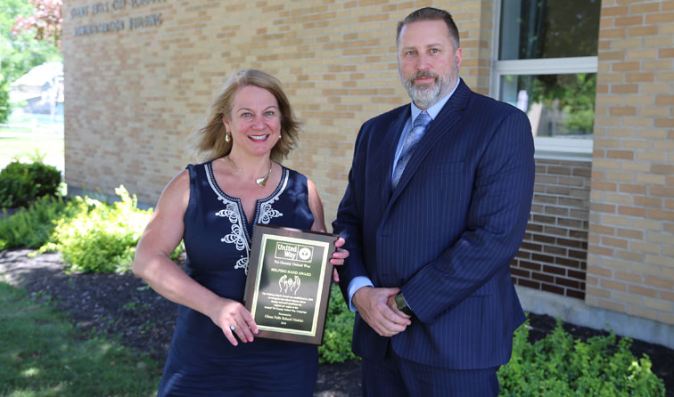 teacher and superintendent smiling outside with United Way Helping hands plaque
