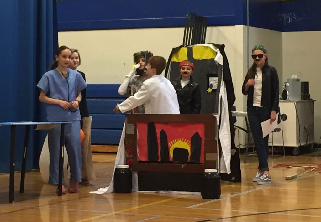 six students in costumes and with a set performing in a gym