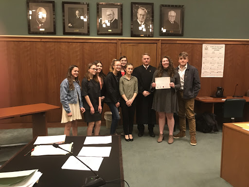 nicne students smiling holding certificate with judge inside courtroom