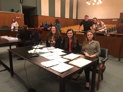 three students smiling at attorney's table inside courtroom