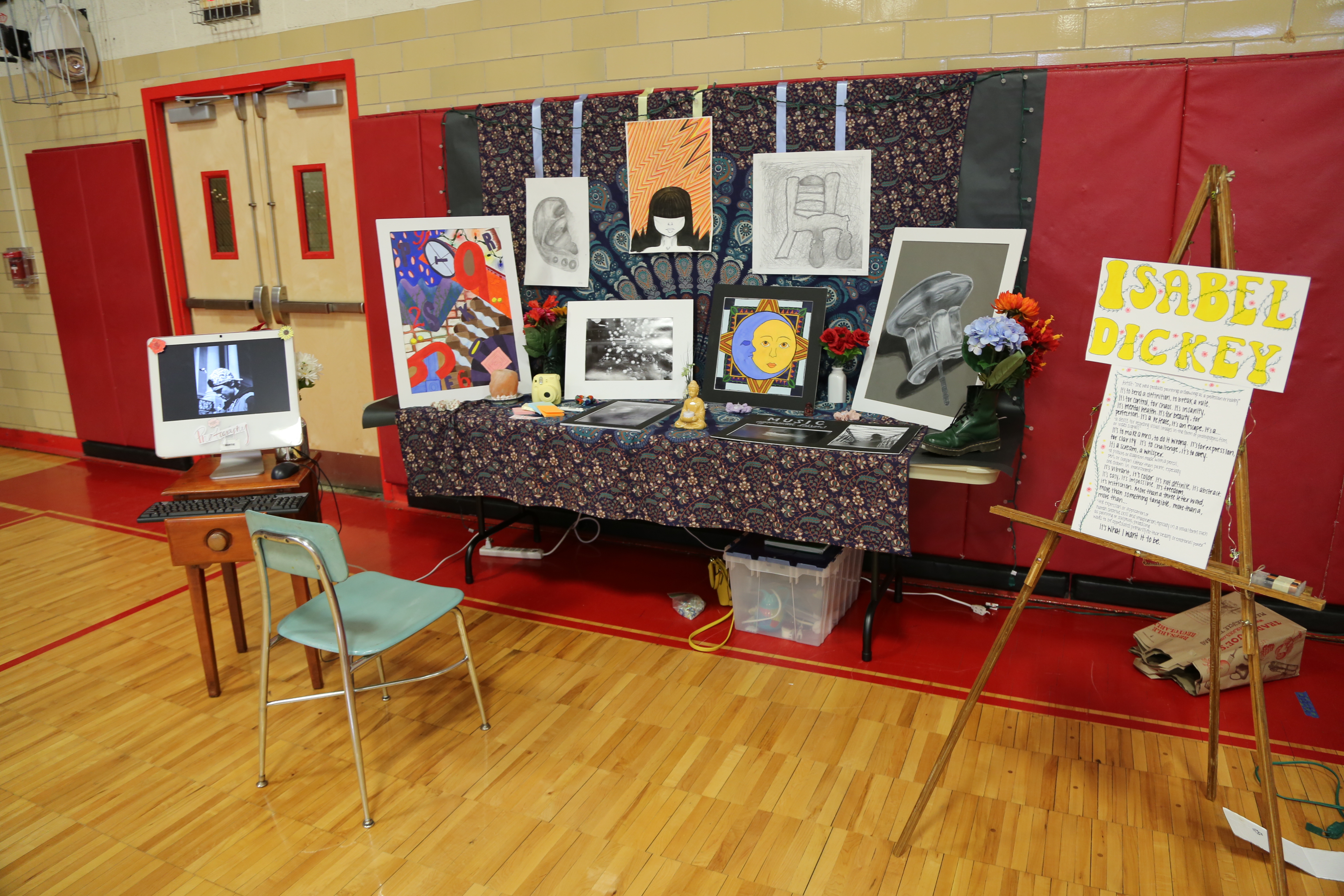 student artwork and paintings on display on a table in a gymnasium