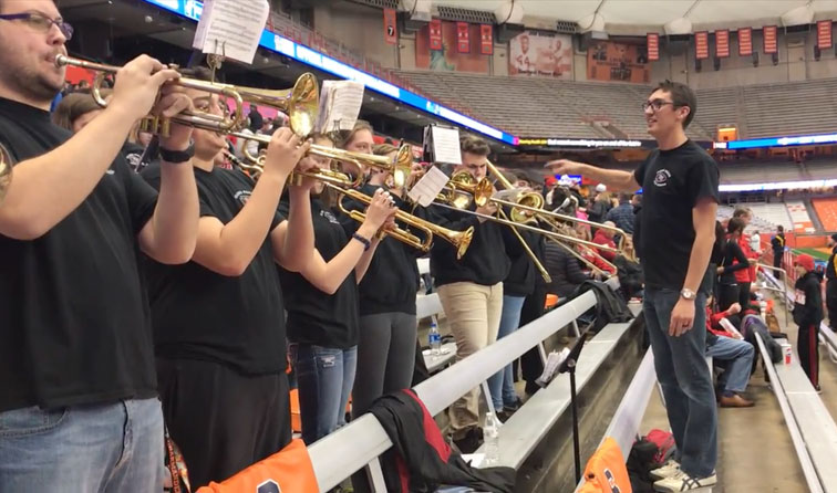 man directing student horn section in sports stadium
