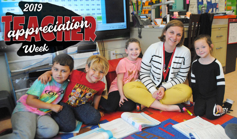 teacher sitting with four elementary students on classroom carpet smiling