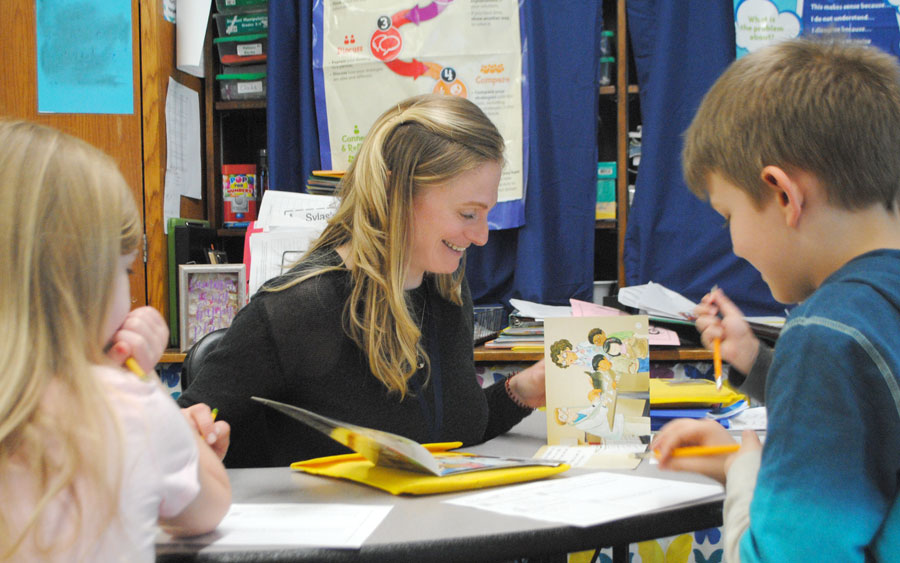 woman smiling while reading with elementary students