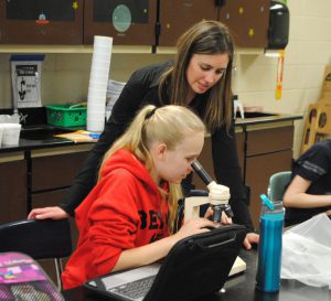 teacher and student looking into microscope in classroom