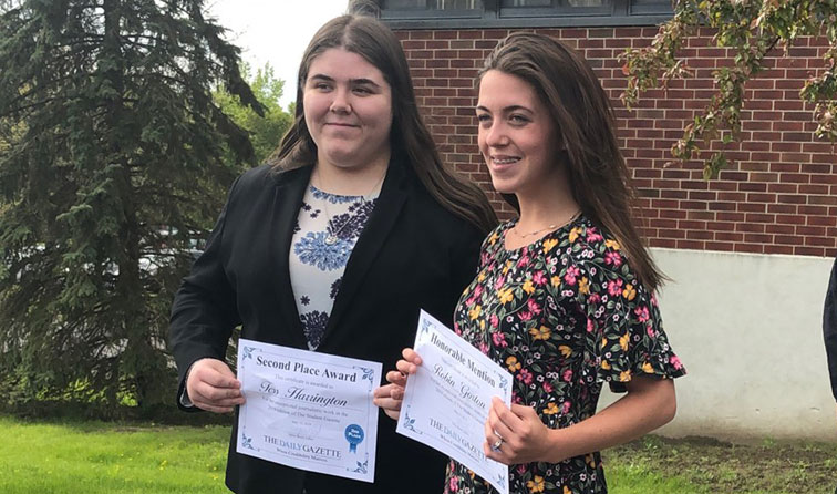 two girls smiling outside holding certificates