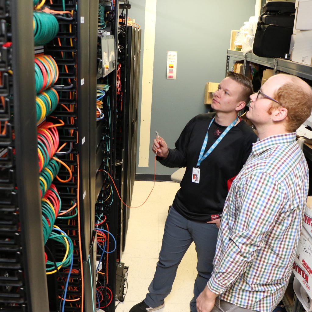 two people examining a server bank with colorful wires