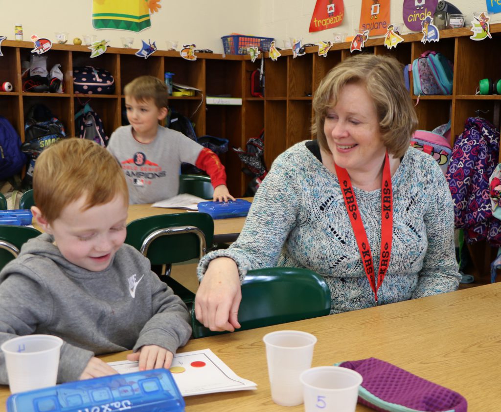 teacher smiling with student working on an activity at small table