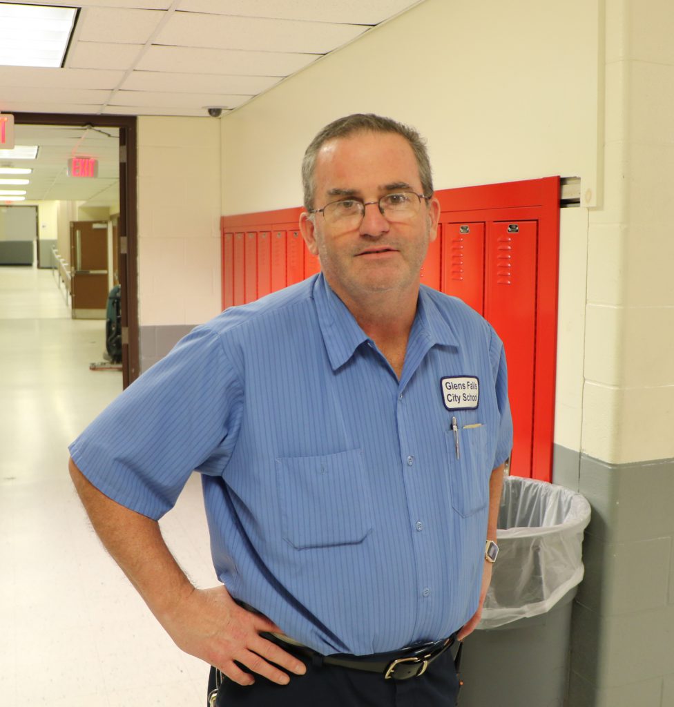 custodian standing in school hallway with red lockers behind