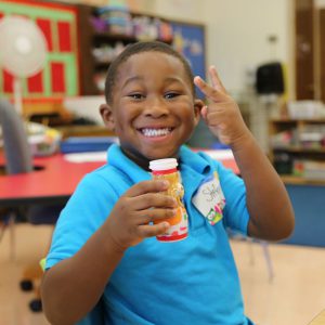 student in kindergarten classroom during snack time smiling with drink