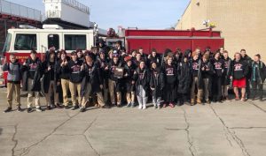 big group of student-athletes in front of fire truck holding sectionals plaque