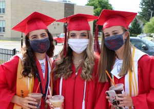 three girls in graduation caps and gowns, wearing face masks