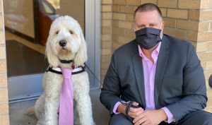 Finnigan the golden-doodle wearing a pink tie, sitting next to Superintendent Jenkins wearing a pink shirt