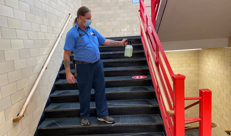 custodian standing on step of school stairwell spraying sanitizer on hand rails