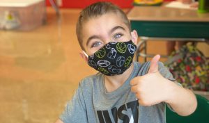student giving a thumbs-up to the camera and wearing a sports-themed face mask