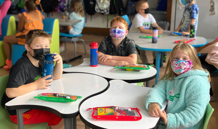 three students wearing masks at a table grouping with new school supplies