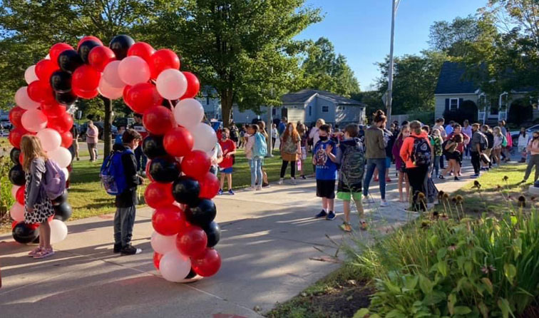 red hite nad black balloon arch with students liked up to walk under on sidewalk on first day of school