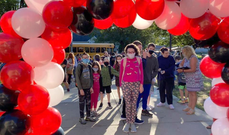 several students standing on the middle school sidewalk with a balloon arch overhead