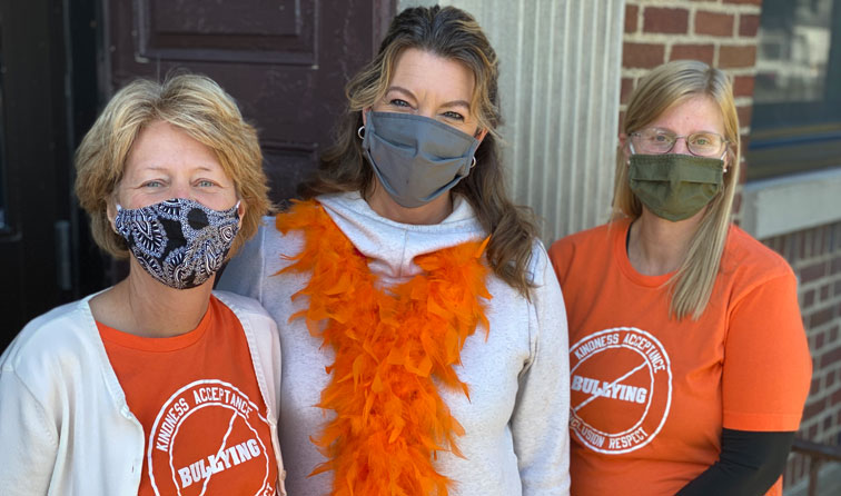 three staff members wearing orange for unity day and smiling under masks