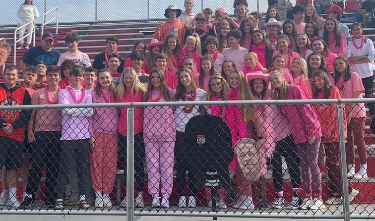 students in football stands smiling and wearing pink for breast cancer awareness