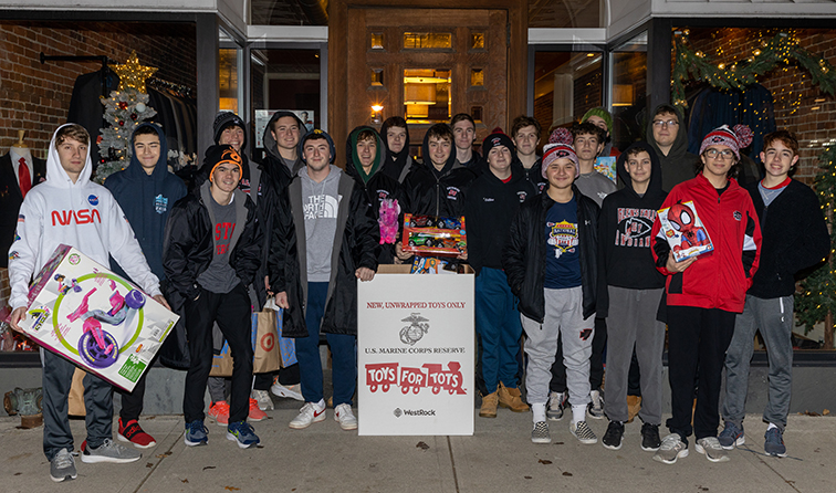 group of students holding toys around a box labeled Toys for Tots