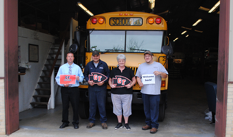 four employees standing in front of school bus holding welcome back signs