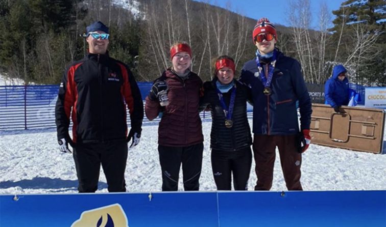 Nordic skiers and coach standing with medals in the snowy sunshine