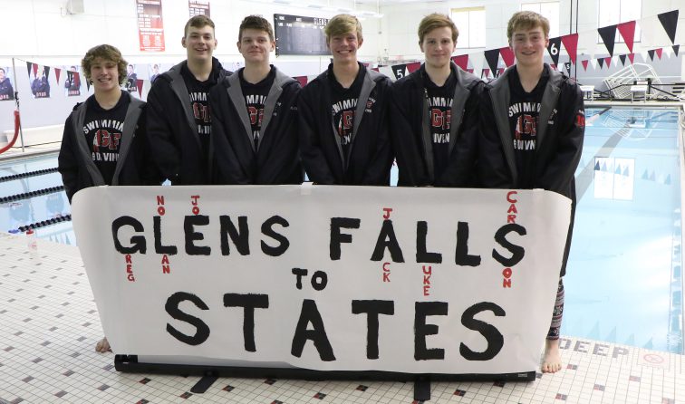 six swimmers in matching jackets standing behind sign reading: Glens Falls to States on pool deck