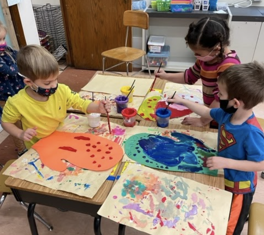 three students painting large pirces of paper with brightly-colored paint