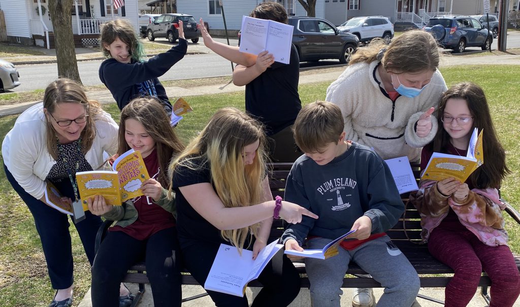 group of students outside in funny poses with the books they're published in