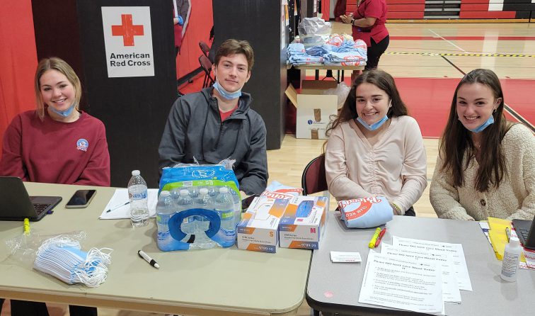 four students smiling at the check-in table for the high school blod drive