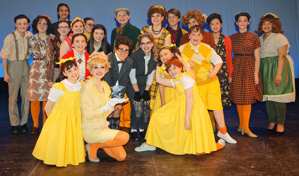 cast members of musical in costume smiling on stage with award trophy