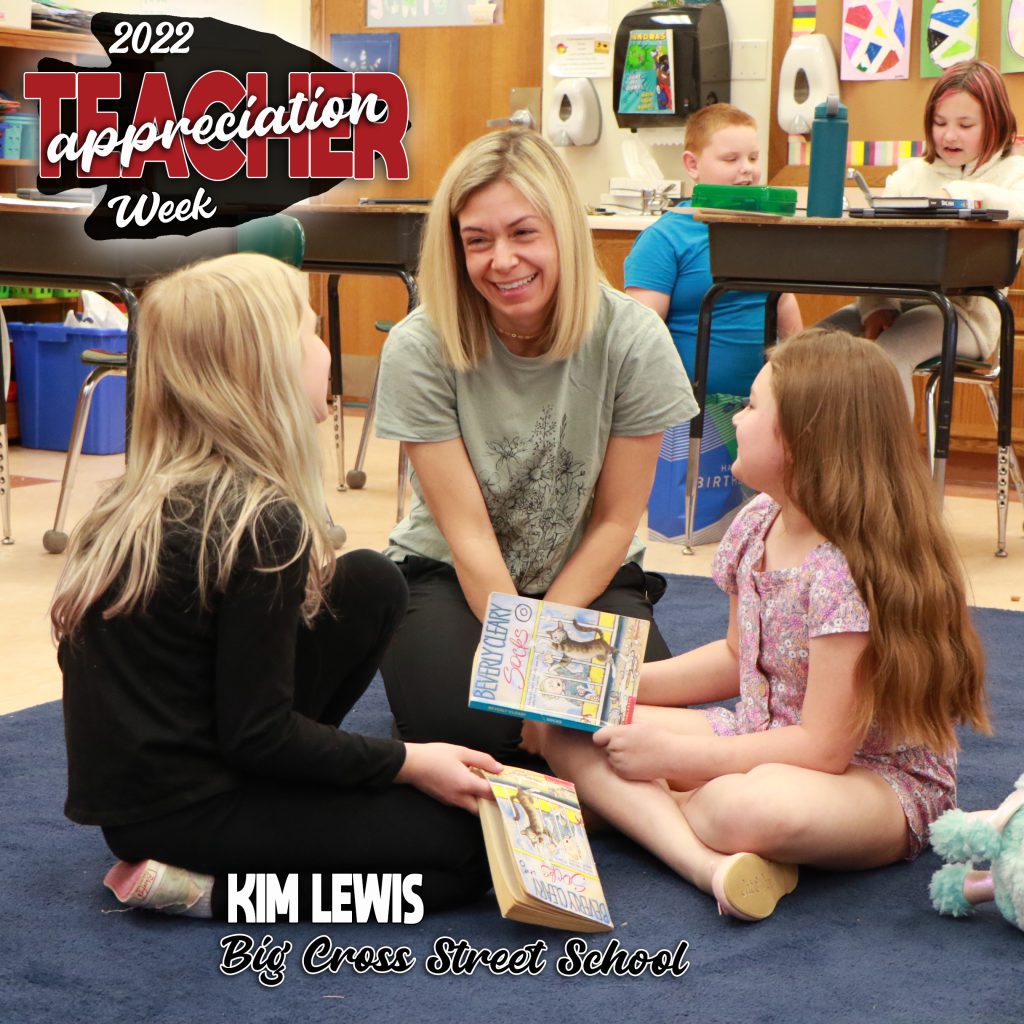 two students and a teacher sitting on a classroom rug discussing their reading books