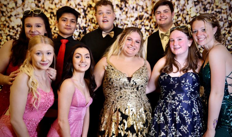 group of students in fancy attire for prom, smiling in front of a sparkly backdrop