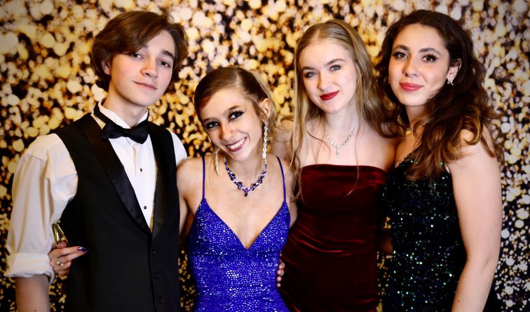 group of students in fancy attire for prom, smiling in front of a sparkly backdrop