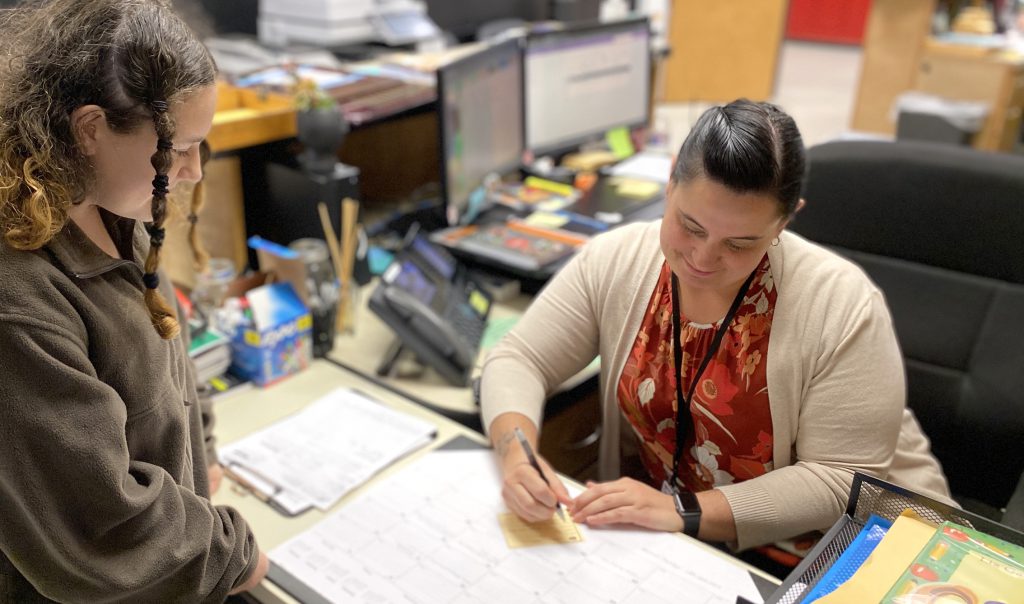 school secretary writing out a hall pass for a student at her desk