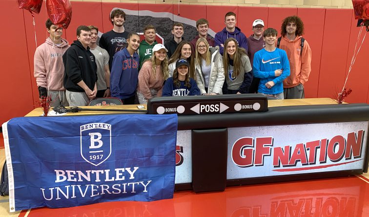 group of students smiling behind a table where an athlete just signed letter of intent to play LAX at Bentley