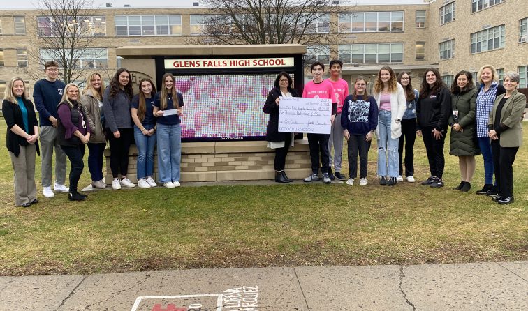 group of students, teachers and hospital foundation representative standing in front to the high school, holding a big check from fundraising efforts
