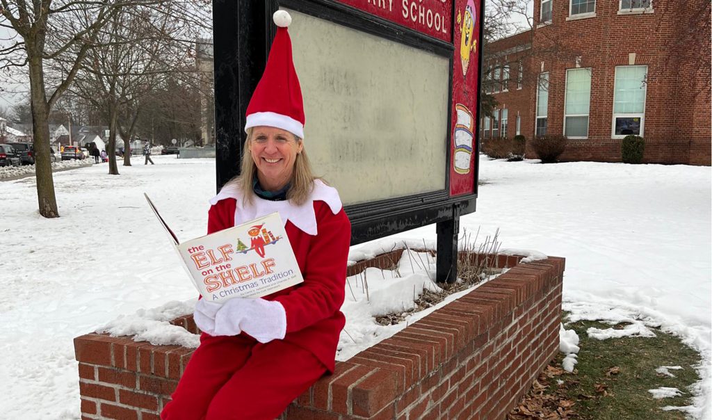 Ms. Mauro the principal dressed as Elf on the Shelf reading the book in front of school