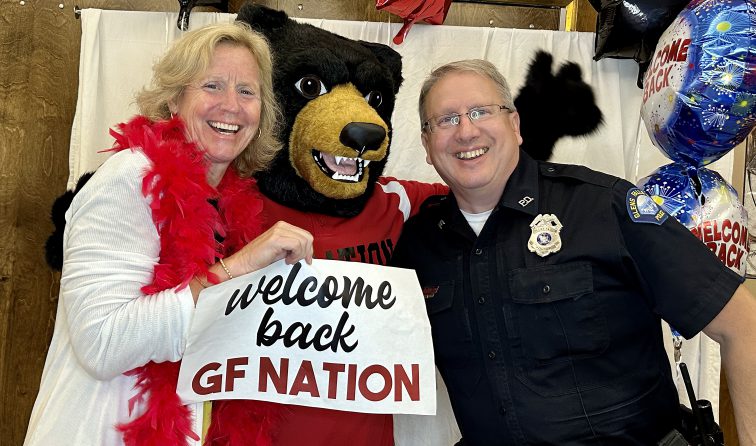 Assistant principal and school resource officer smiling with the Black Bear mascot and holding a sign reading welcome back GF Nation