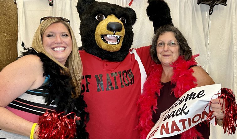 two people smiling and holding red metallic pom-poms with the Black Bear mascot