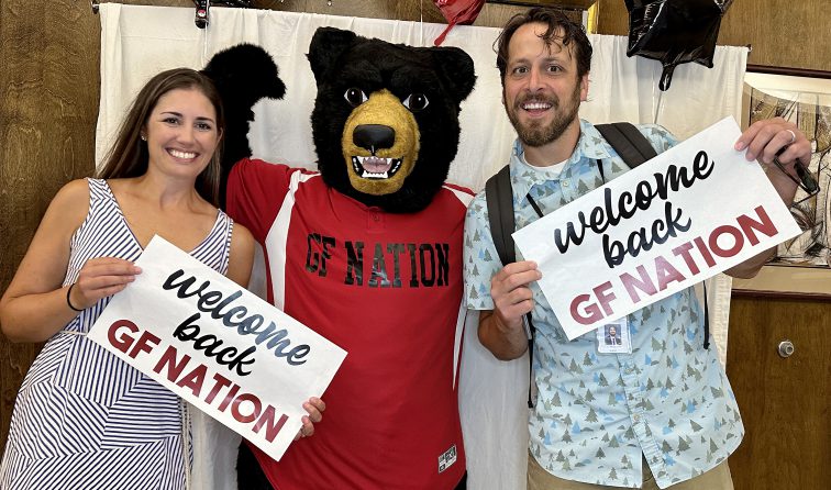 Two GFMS teachers holding welcome back signs with the Black Bear Mascot flexing in the background