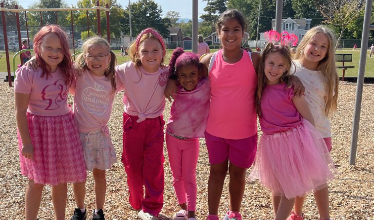 group of elementary students dressed in pink for breast cancer awareness, outside on the playground smiling