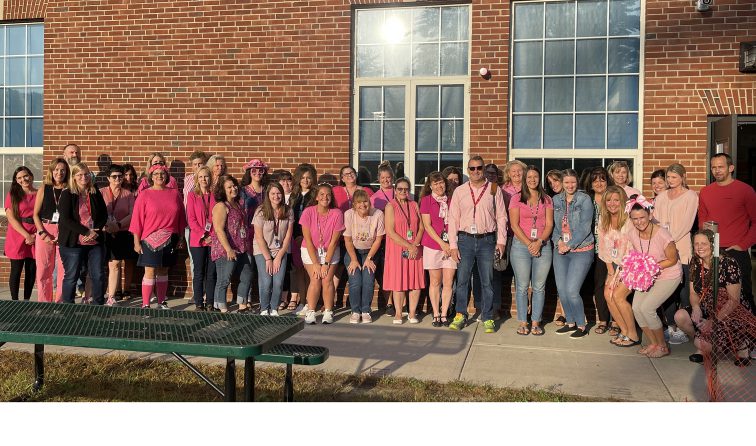 large group of school staff members all wearing pink for breast cancer awareness outside the school building